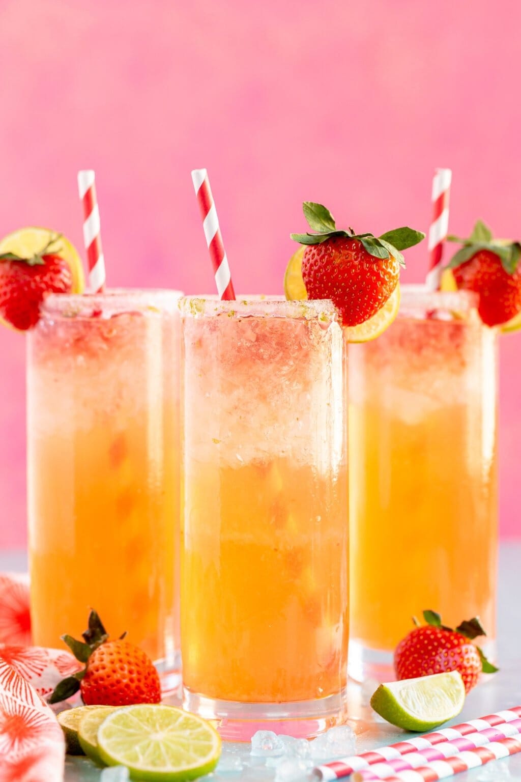 Three glasses of strawberry lemonade with fresh strawberries and a slice of lime on the rim.