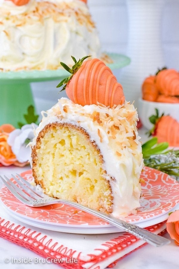 Slice of Bundt cake coated with coconut cream and topped with a strawberry shaped frosting. 