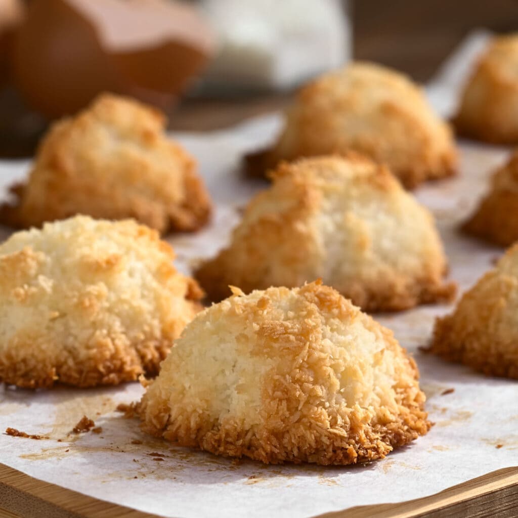Closeup of coconut macaroons arranged on top of a wooden board with baking sheet.