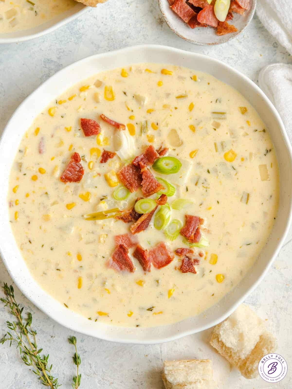 Corn chowder on a bowl topped with bacon beets and chopped onion leaves. 