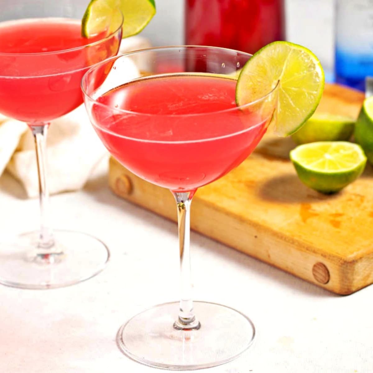 Two glasses of homemade cosmopolitan cocktail with limes on a cutting board in the background
