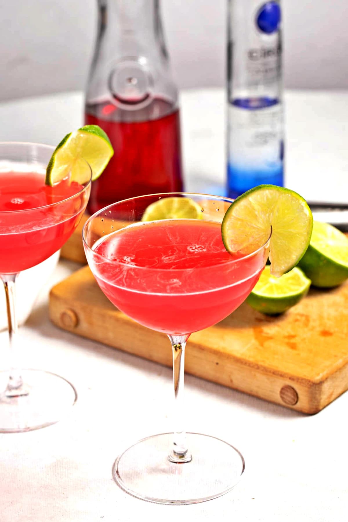 Two cosmopolitan cocktails with lime and cranberry juice and lime halves in the background