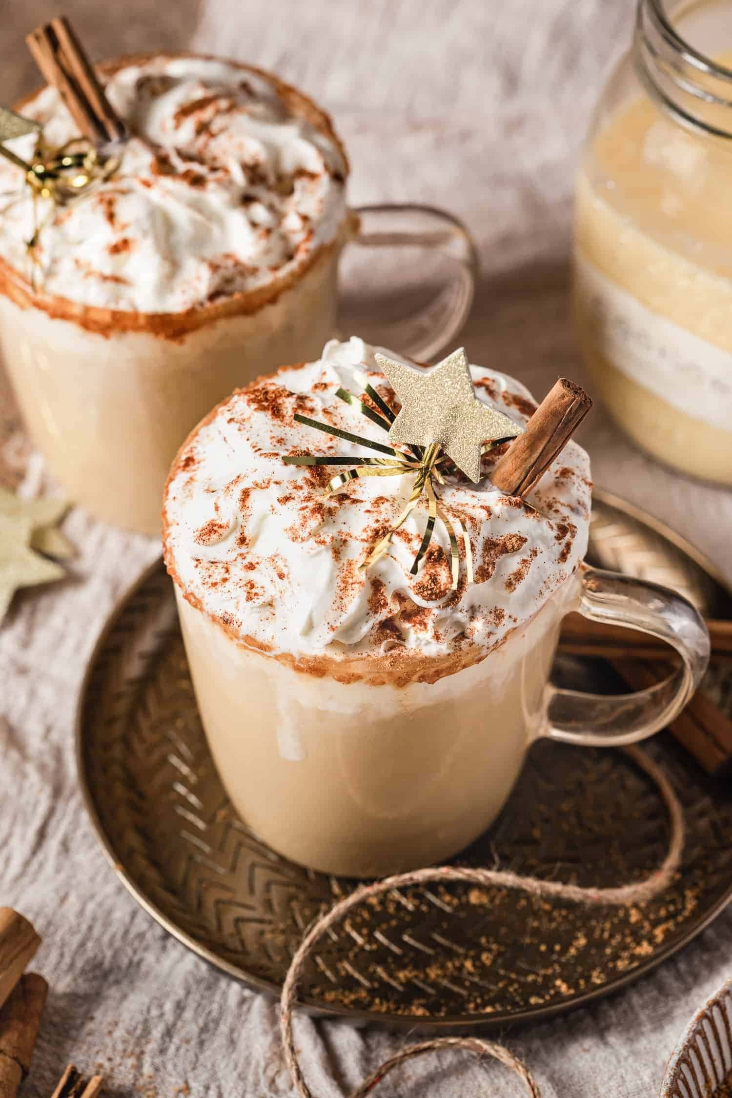 Servings of eggnog latte topped with cream and cinnamon powder and sticks.