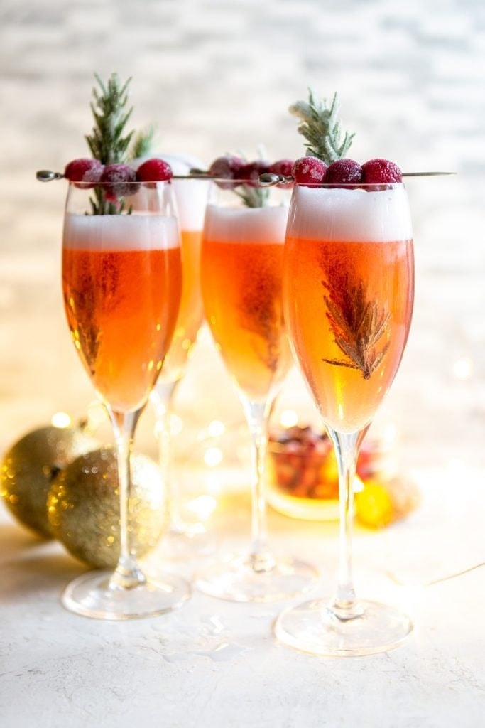 Cranberry mimosa cocktail on wine glasses garnished with cranberries and rosemary.