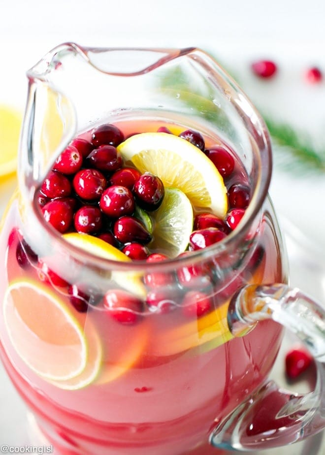 Top view of a glass pitcher with slices of lemon and cranberries.