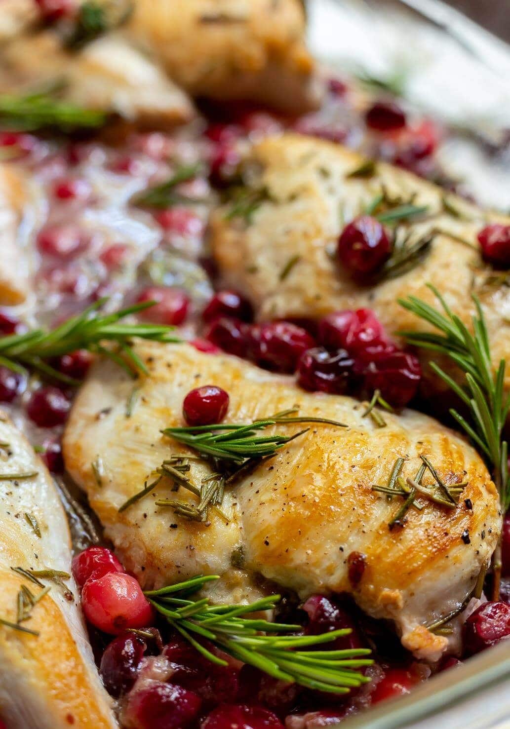 Seasoned baked chicken breast with cranberries and rosemary on a baking pan.