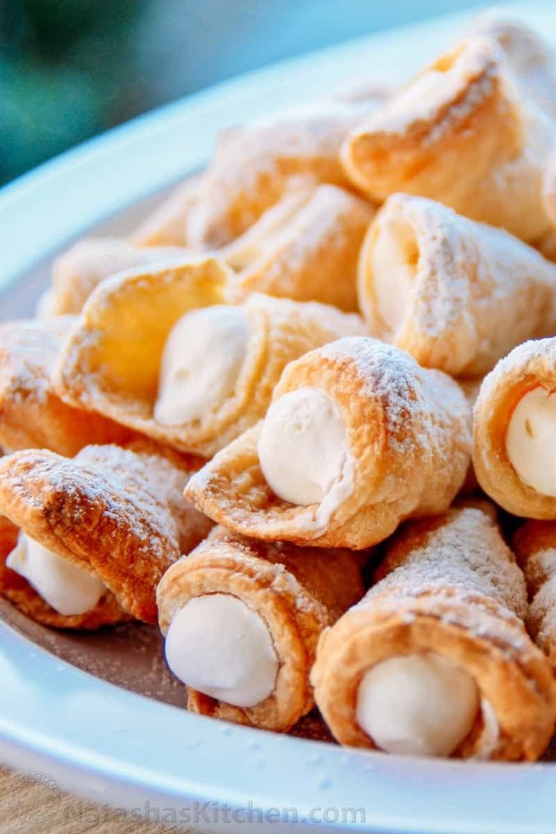 A bunch of cream-filled pastry sprinkled with powdered sugar on a plate.