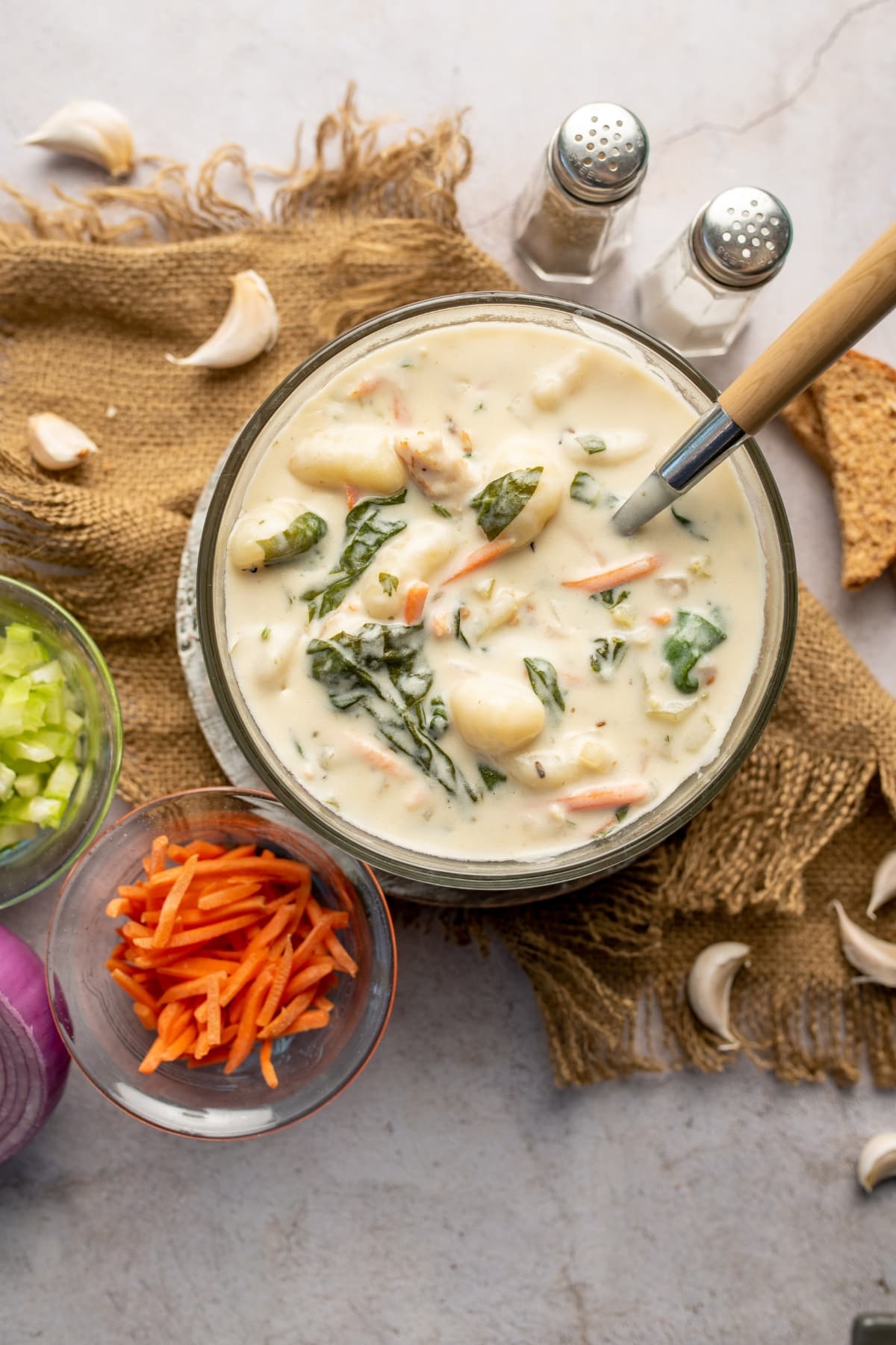 Olive Garden Chicken and Gnocchi Soup (Copycat) featuring Chicken and Gnocchi Soup with Veggies in a Bowl with a Spoon on Top of Burlap Cloth with Ingredients All Around