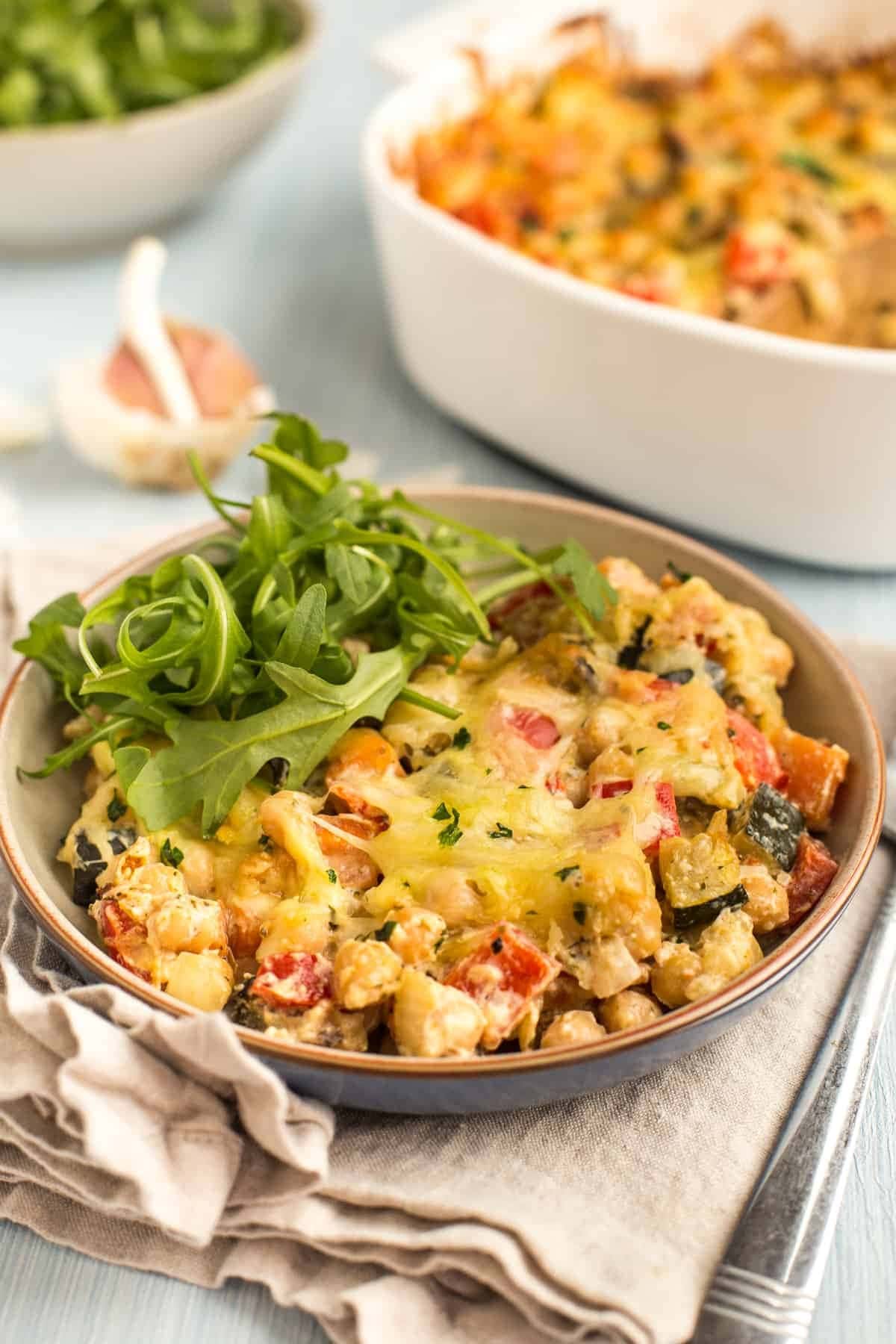 Creamy Chickpea Bake on a saucer with fresh arugula leaves on top