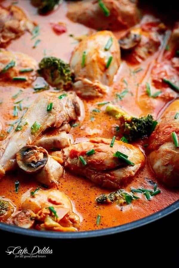 Chicken drumsticks, mushrooms, and broccoli baked in a creamy tomato sauce on a skillet.