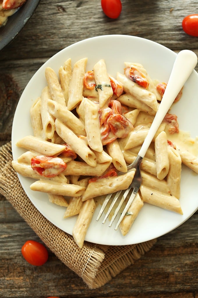 Creamy pasta with garlic and roasted tomatoes on a white plate.