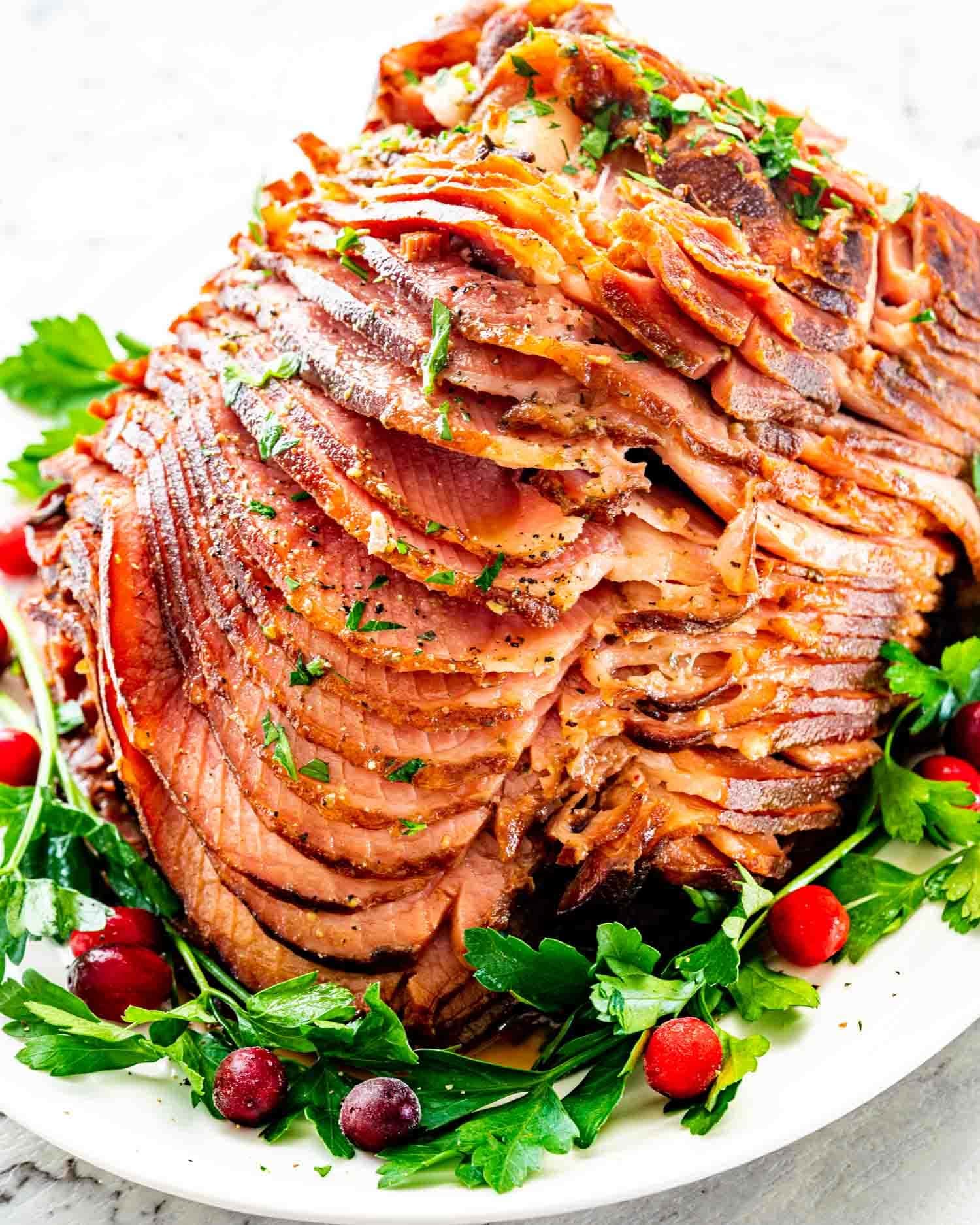 Thinly sliced honey mustard glazed ham garnished with cherries and parsley leaves.