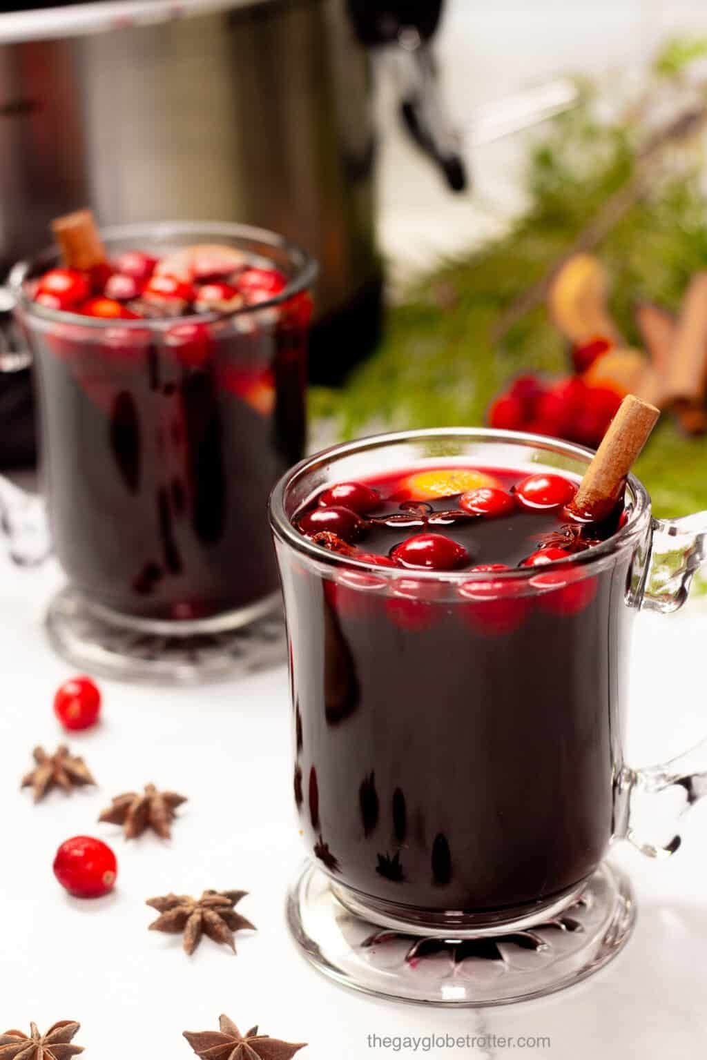 Two glasses of mulled wine with cherries and cinnamon stick garnish.