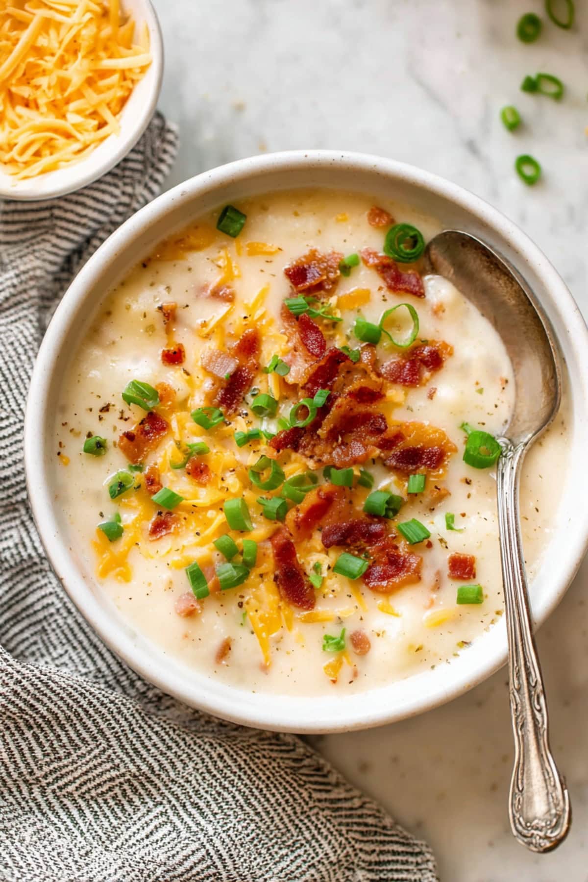 An overhead view of a bowl of potato soup with green onions, cheese and bacon bits.