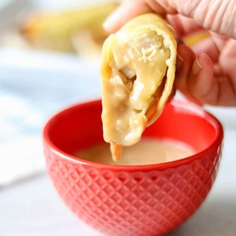 Egg roll dipped in gravy from a red bowl. 