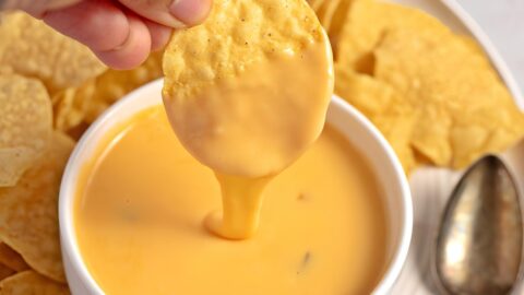 A person dipping chips into a bowl of nacho cheese sauce