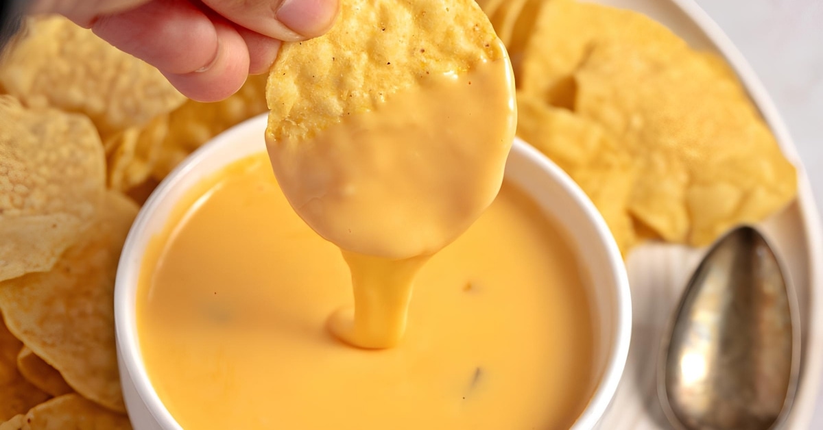A person dipping chips into a bowl of nacho cheese sauce