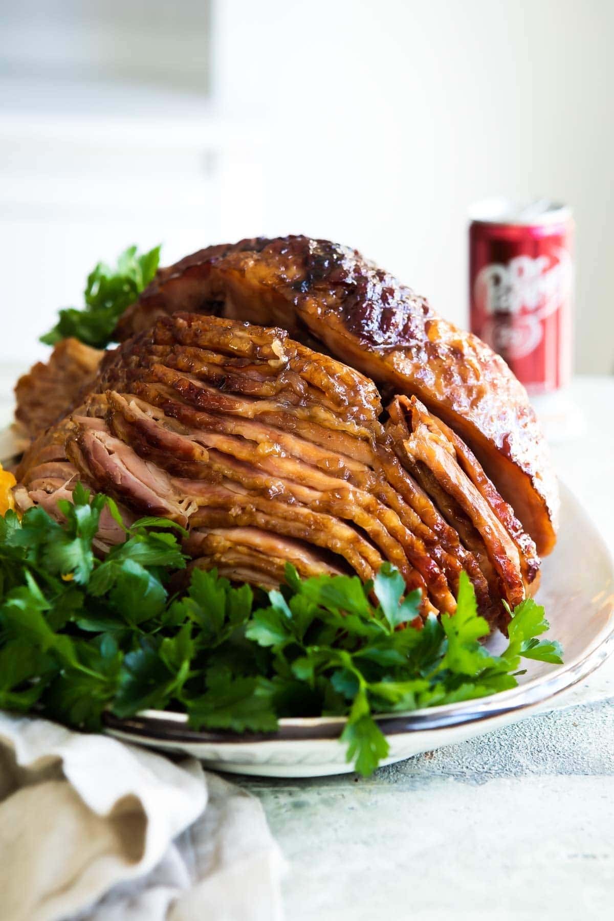 Thinly sliced glazed ham garnished with parsley leaves and a can of Dr. Pepper in the background.