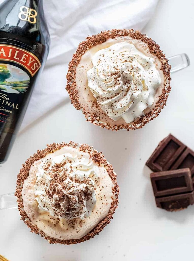 Chocolate rimmed cocktail topped with whipped cream and a sprinkle of cocoa powder and a bottle of Bailey's beside.