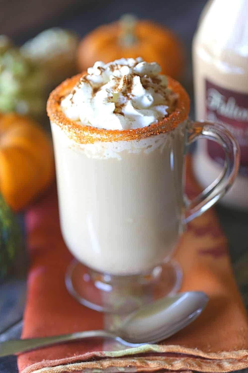 Pumpkin spice latte on a spice-rimmed glass mug topped with whipped cream. 
