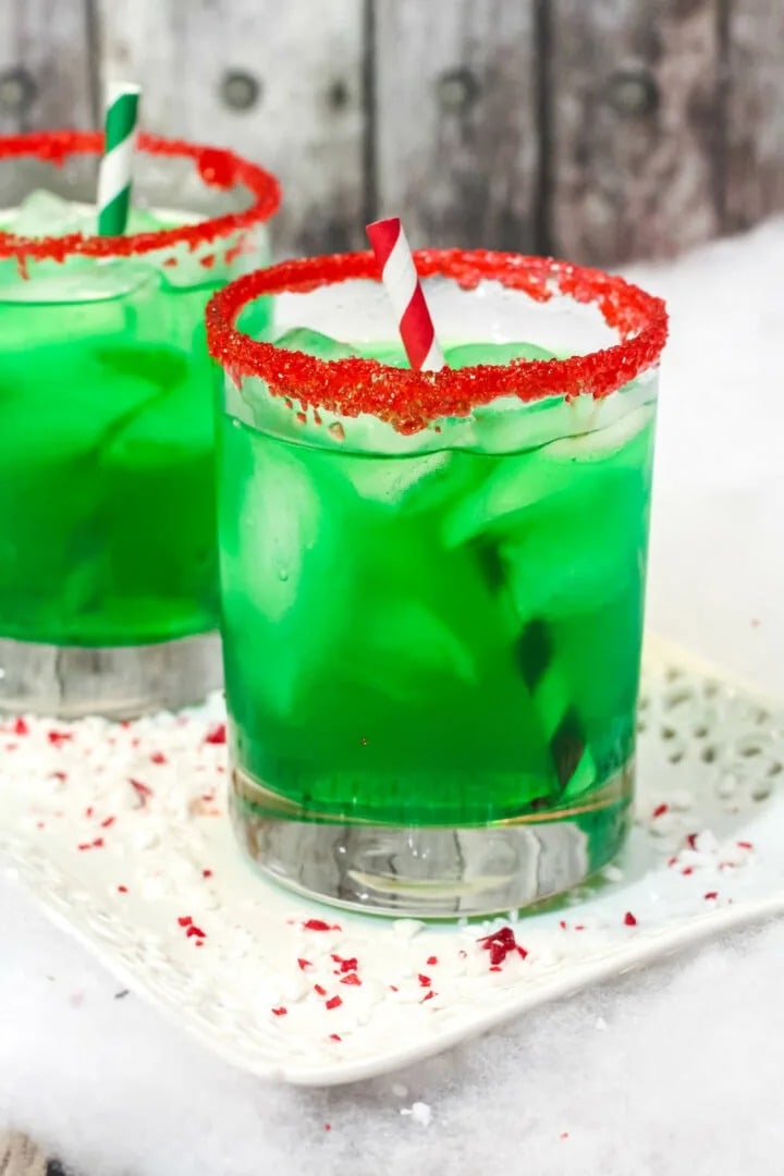Two red-rimmed glasses of green punch drinks with straw. 