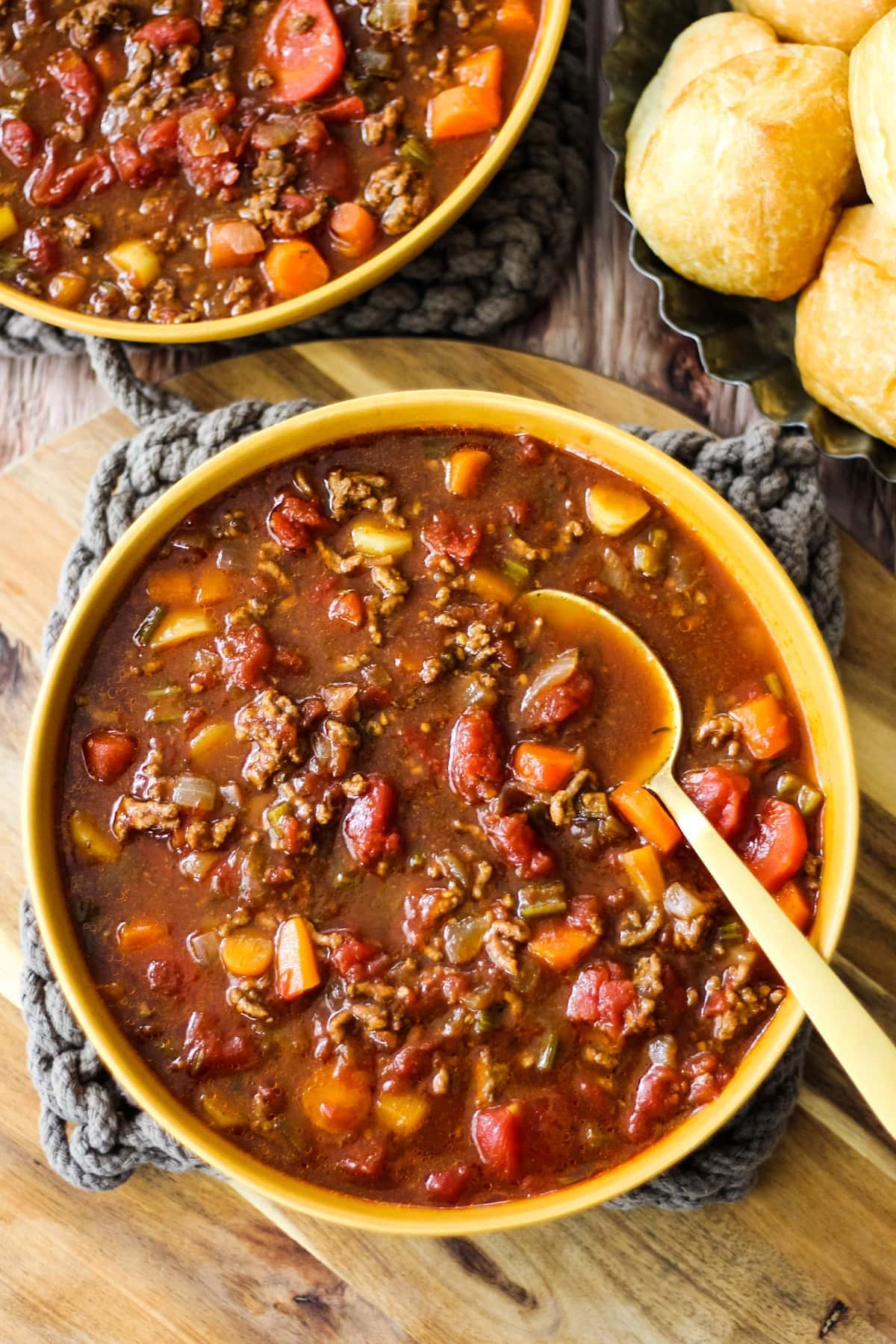 Hamburger soup with ground beef, beans, carrots, tomatoes and potatoes in a bowl with a spoon- top view
