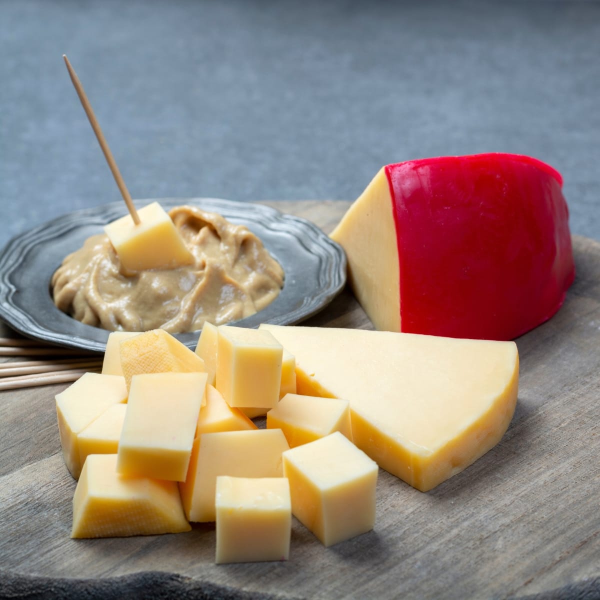 Edam Cheese Block and Chunks with Dip on a Gray Cutting Board and Gray Background