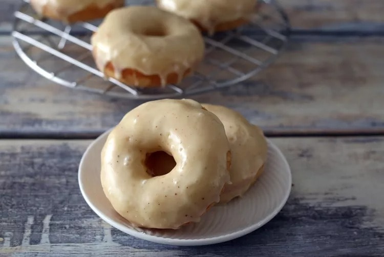 Doughnuts topped with eggnog glaze on a cooling rack and plate. 