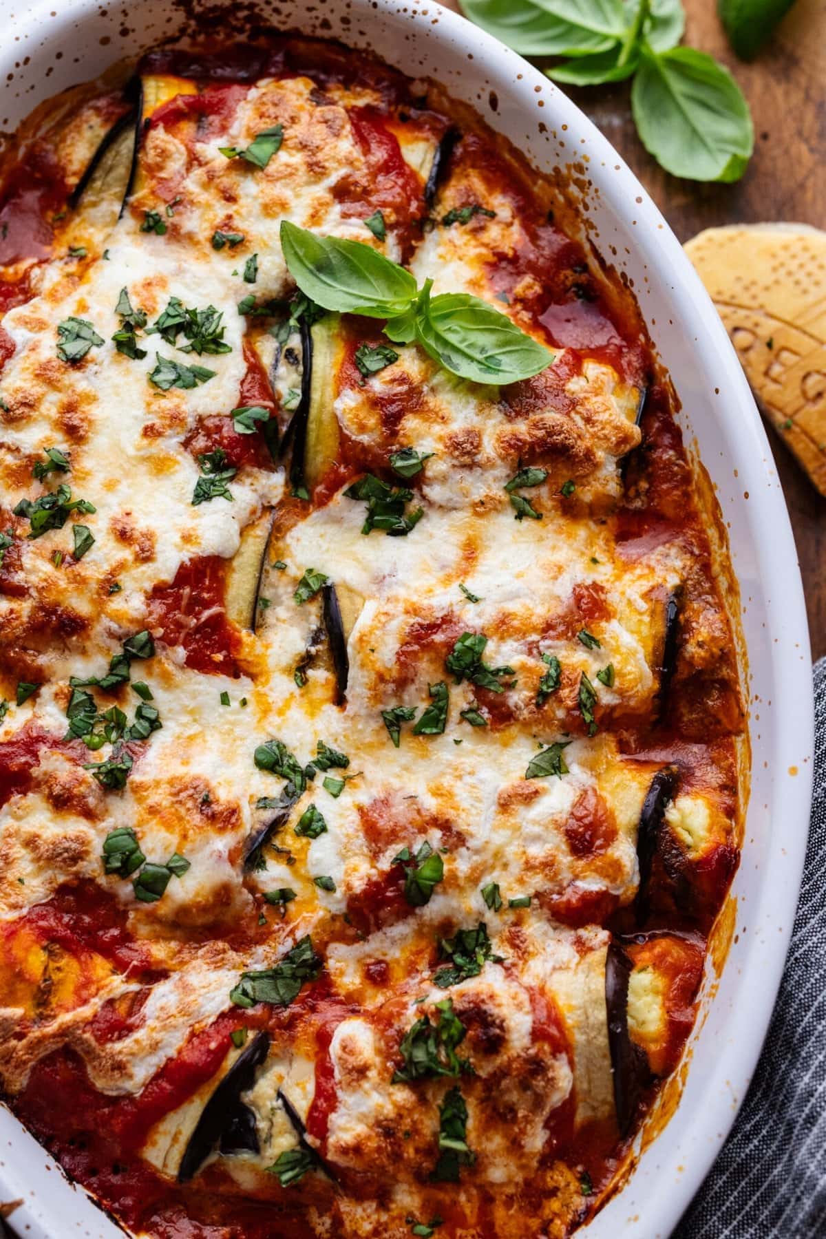 Baked eggplant rollatini in a casserole dish made with thinly sliced eggplant gets rolled up and stuffed with Ricotta, Parmesan, and basil.