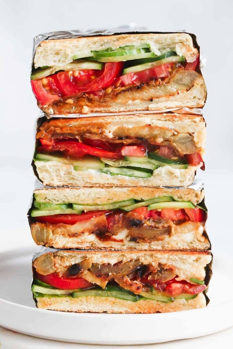 A tower of slice in half sandwich with eggplant, cucumber, tomato and dressing filling. 