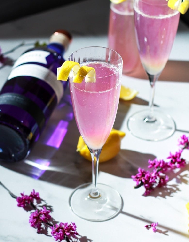 Pink and purple spritz champagne cocktail on  wine glasses with orange peel garnish.