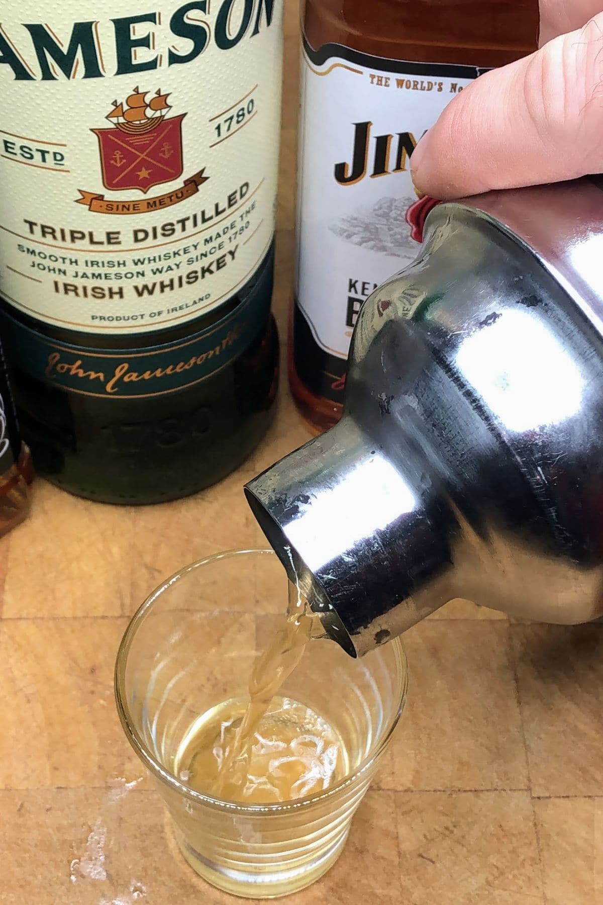 Homemade boozy four horsemen whiskey cocktail being poured from the shaker into a shot glass