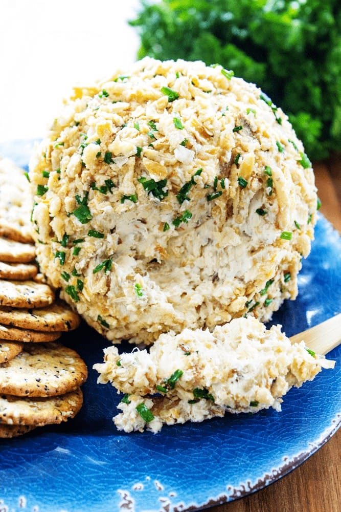 Cheeseball coated with fried onion and chive mixture served with cracker on a plate.