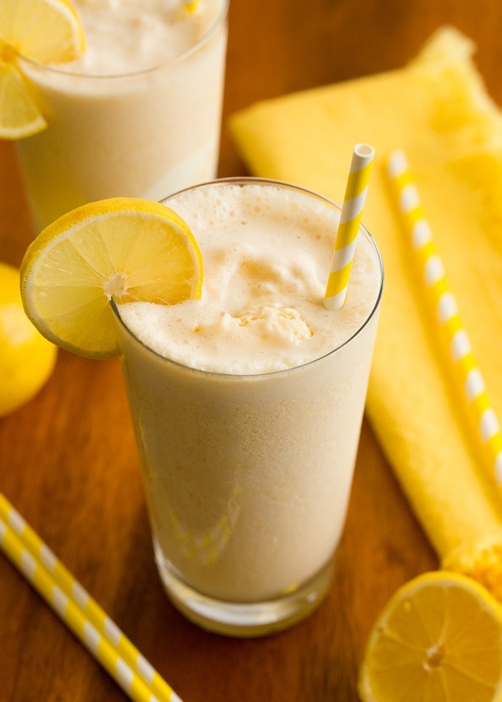 Two glasses of creamy lemonade with straws and lemons.