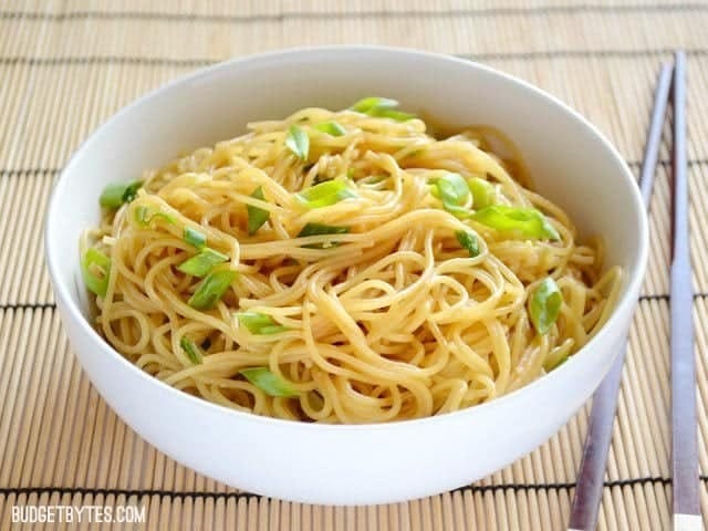 Garlic noodles served on white bowl garnishes with chopped green onions. 