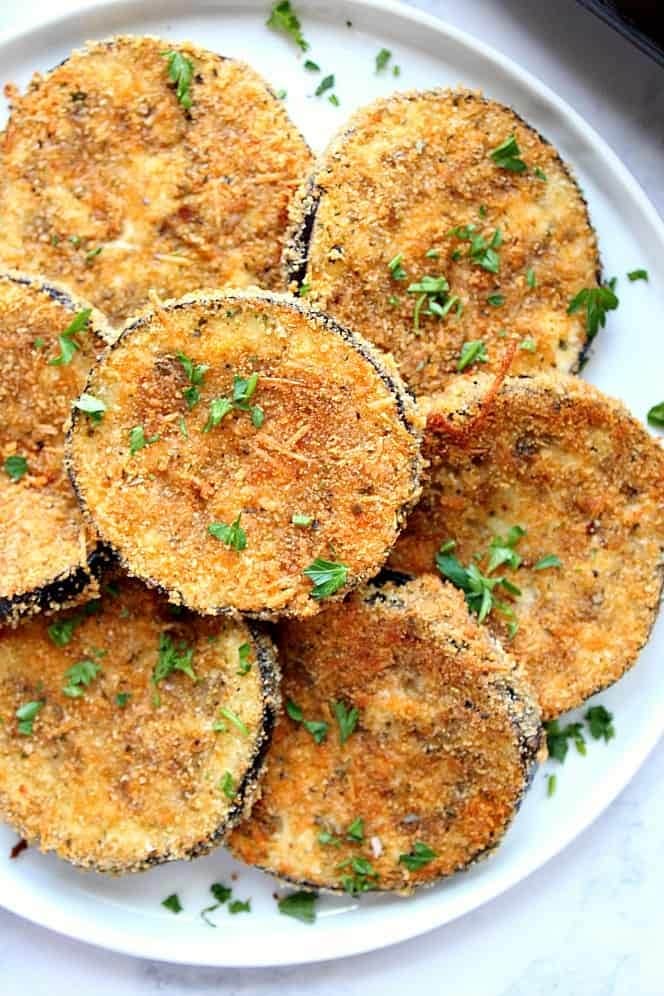 Breaded baked eggplant slices with parmesan cheese garnished with chopped parsley on a plate. 