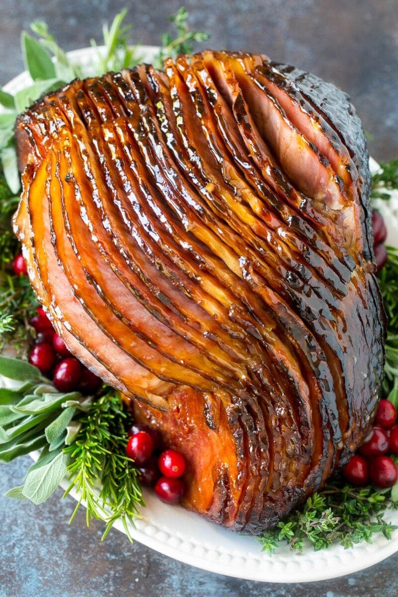 Whole glazed ham coated in a sweet brown sugar and honey glaze served on a festive holiday plate garnished with cranberries and rosemary.