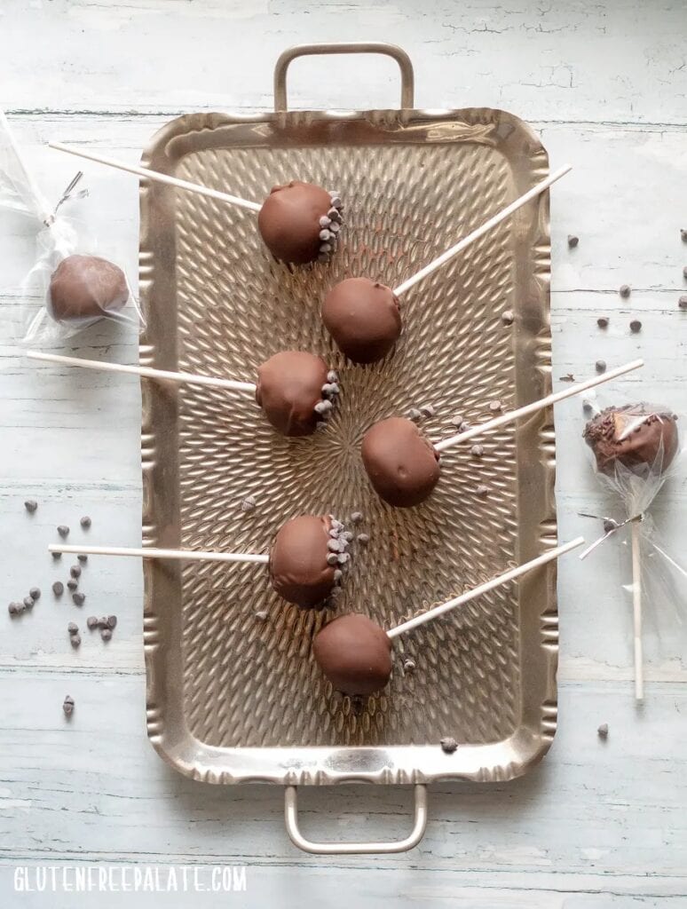 Chocolate covered cake pops with pieces of chocolate chips on a tray.