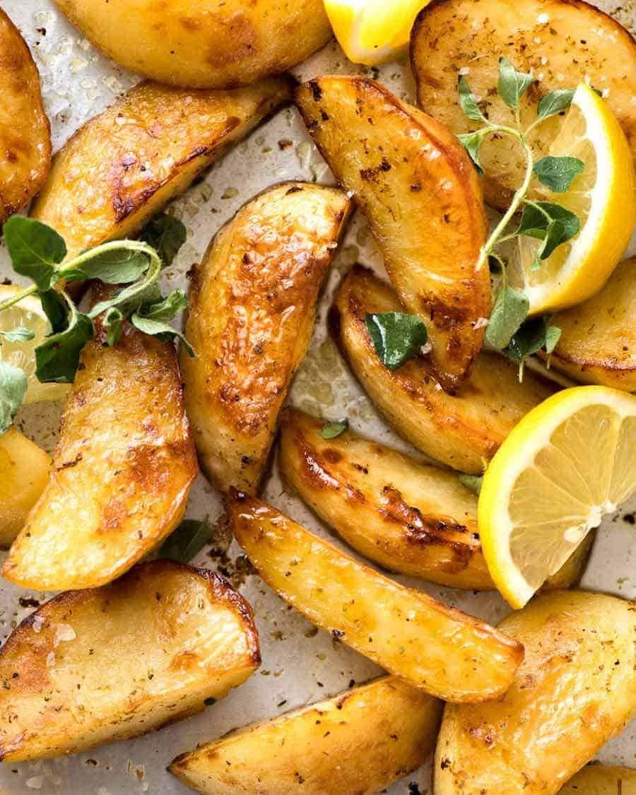 Potato wedges with lemon slices seasoned with herbs and spices on a parchment paper,