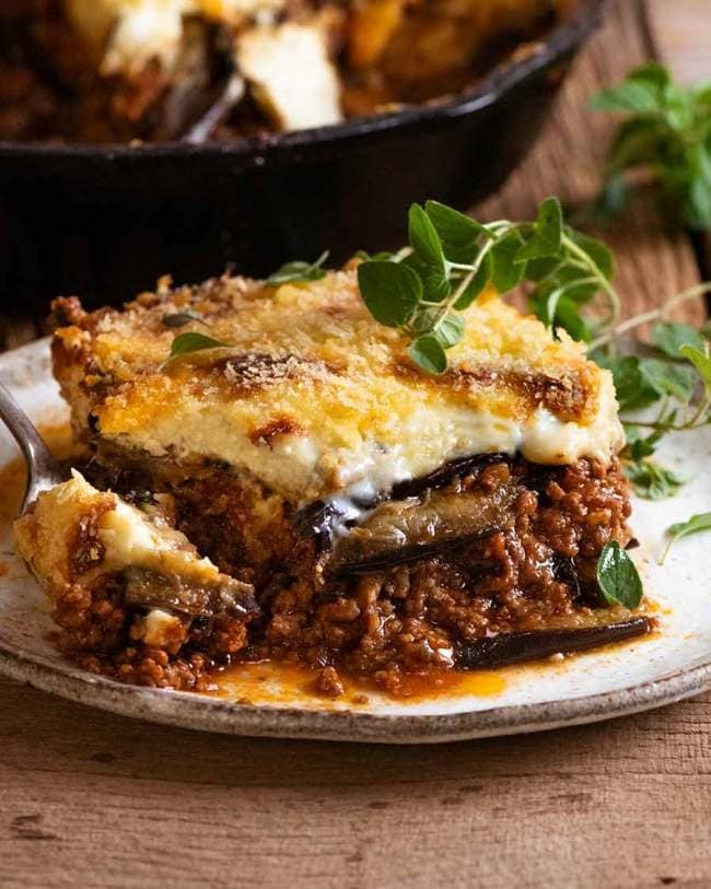 Large piece of Greek Eggplant Lasagna with Layers of Seasoned Beef, Eggplants, and Gooey Cheese on a Plate with a Fork Taking a Bite