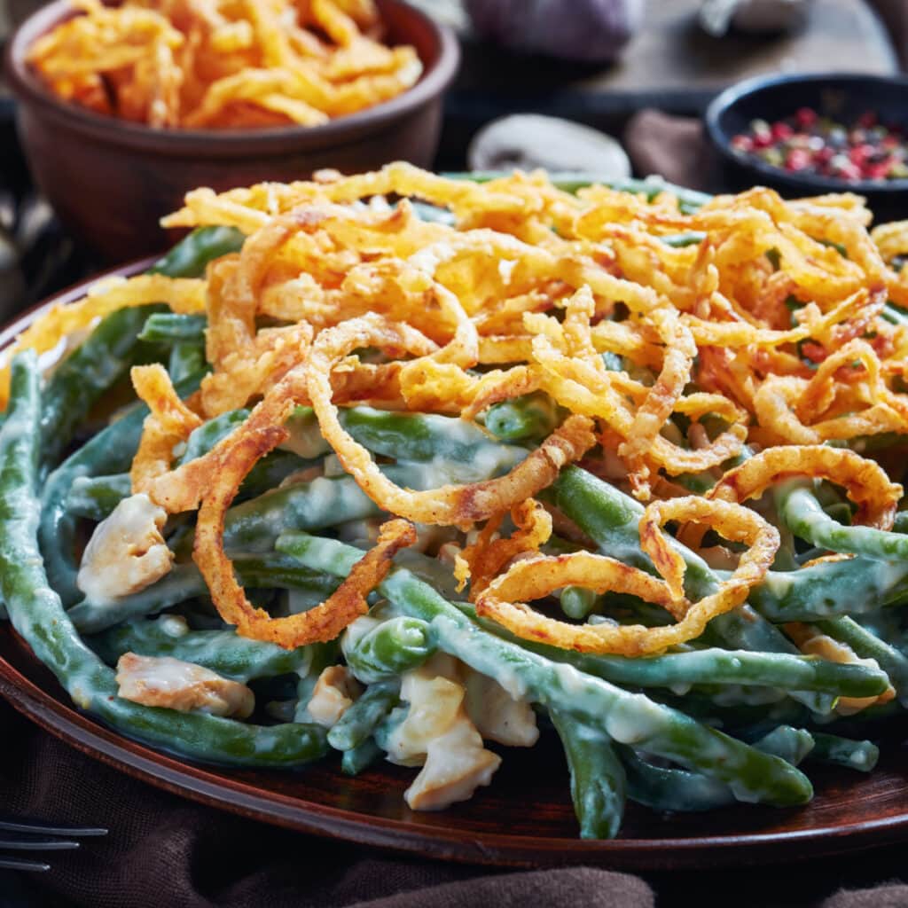 Serving of cheesy green bean casserole in a plate topped with fried onions.