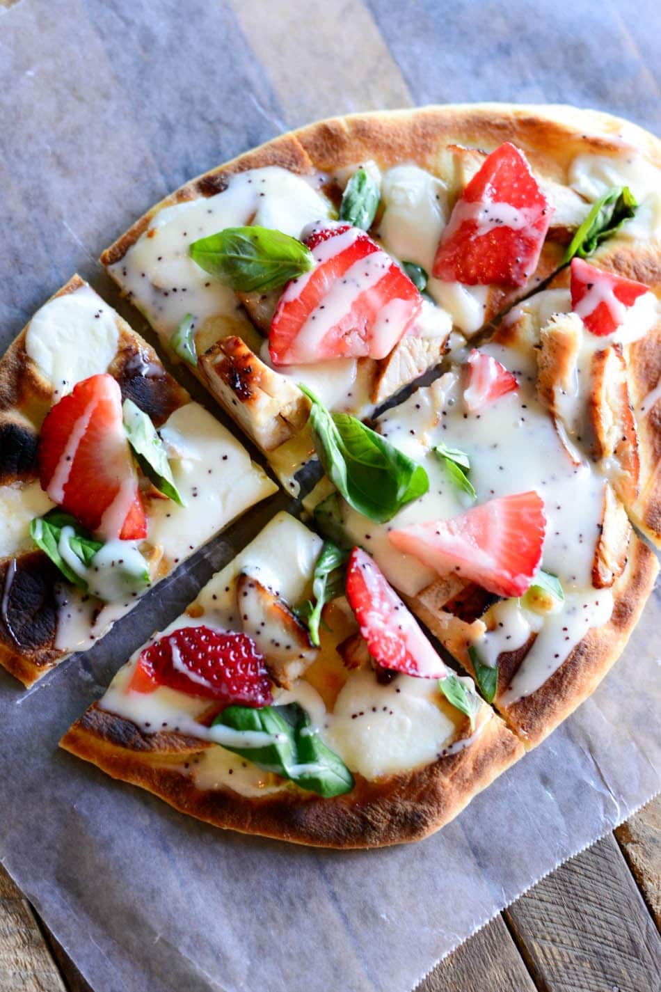 Sliced Grilled Chicken Strawberry Pizza garnished with basil leaves on a parchment paper