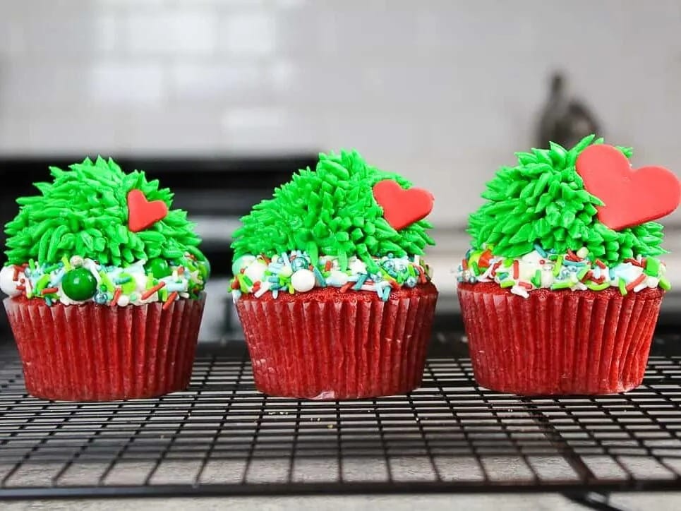 Red cupcakes topped with green frosting and decorated with sprinkles and candies. 