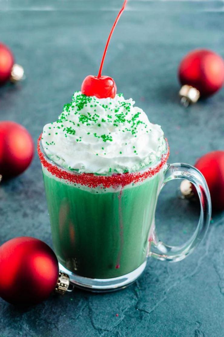 Green colored chocolate drinks on a glass mug topped with whipped cream and  fresh cherry. 