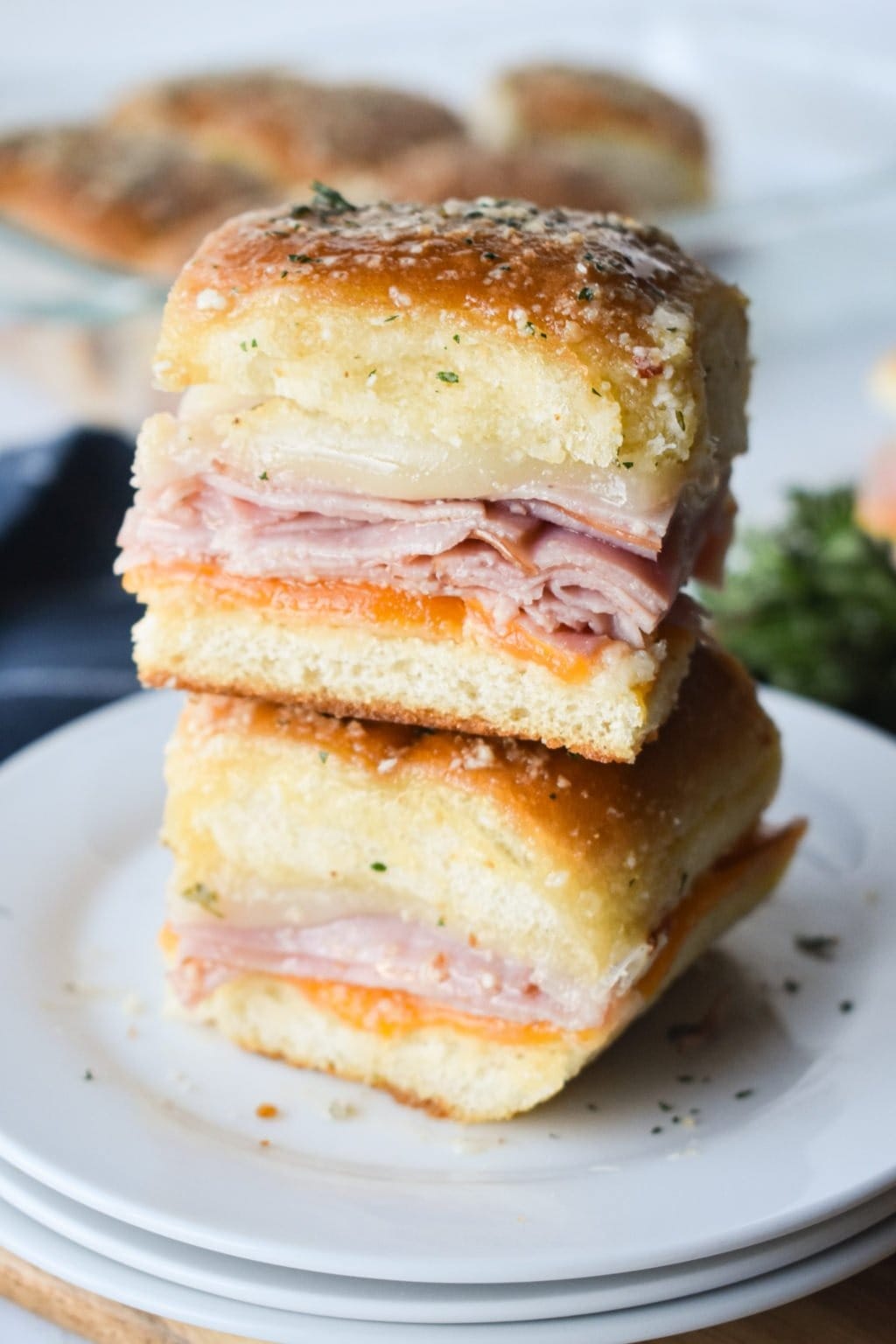 Stack of ham and cheese sandwiches drizzled with parmesan cheese and herbs. 