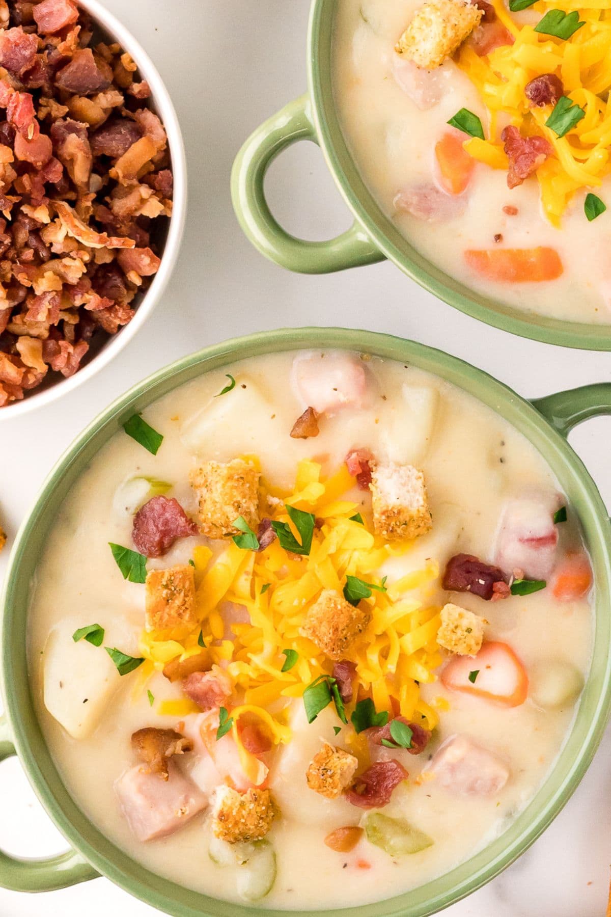 Ham and potato soup served in green bowls and garnished with cheese and bacon bits, top view