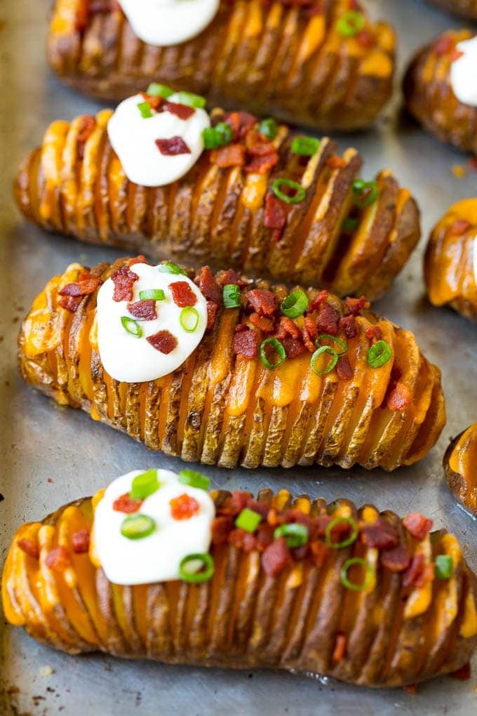 Hasselback potatoes topped with bacon bits and cream on a sheet pan.