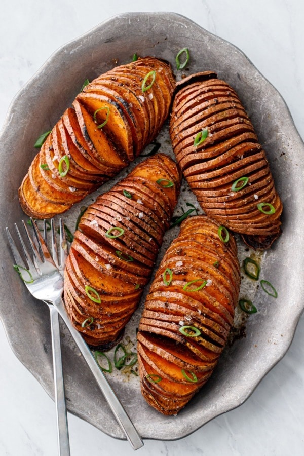 Hasselback sweet potatoes on a stone bowl topped with sprinkles of herbs. 