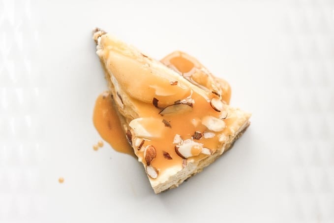 A piece of cheesecake with nuts and caramel sauce on top.