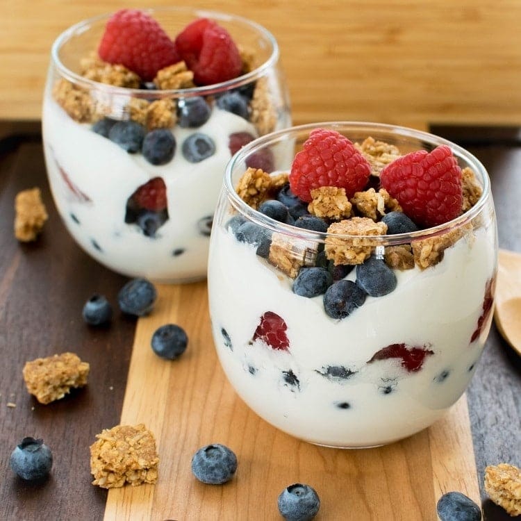 Two glasses of yogurt parfait with sliced bananas, berries and granola.